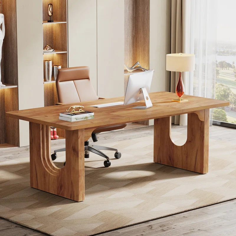 A sleek white executive desk with sculpted panel legs in an office setting, with an office chair and lamp in the background.