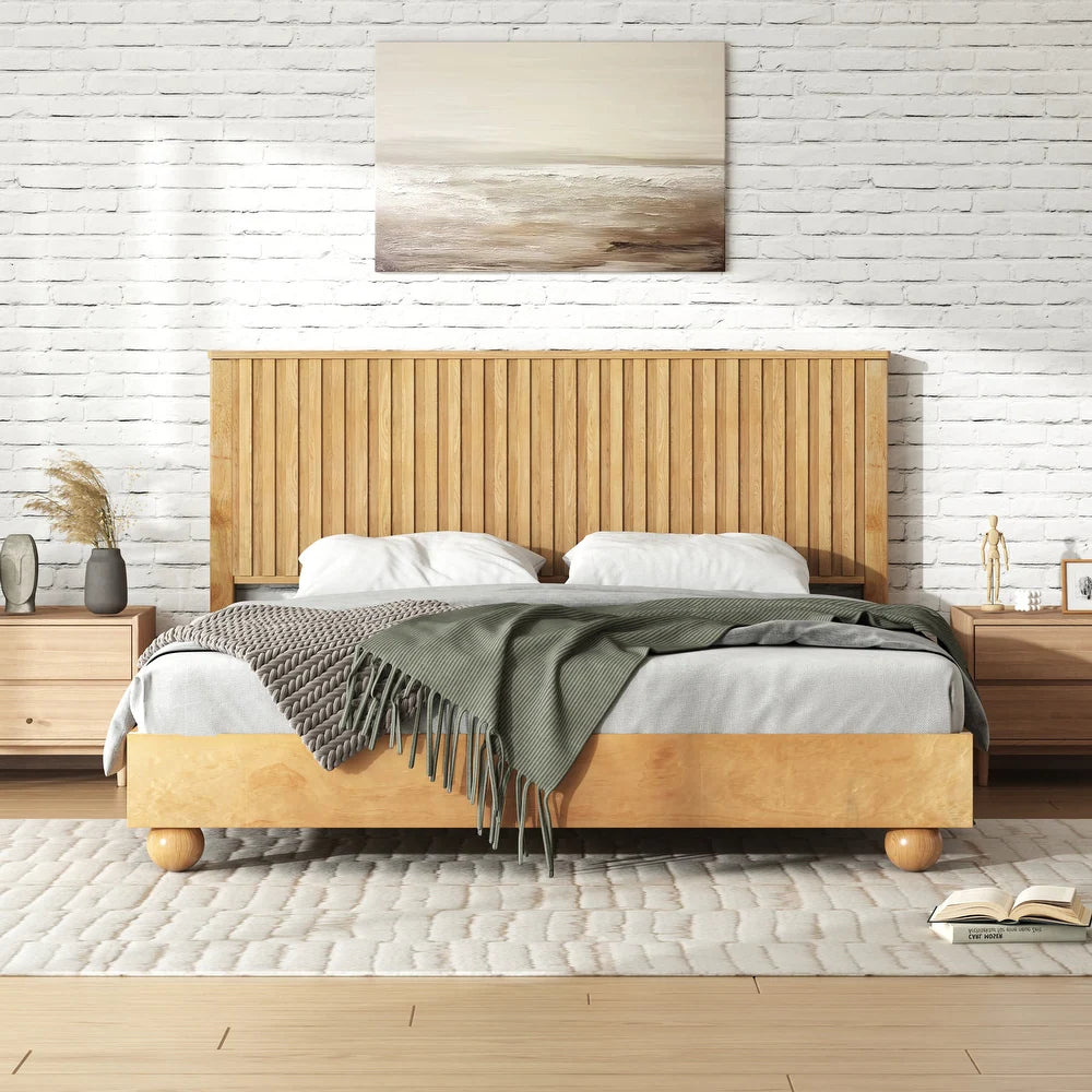 Wooden bed with a green blanket in a room with a white brick wall and wooden floors.