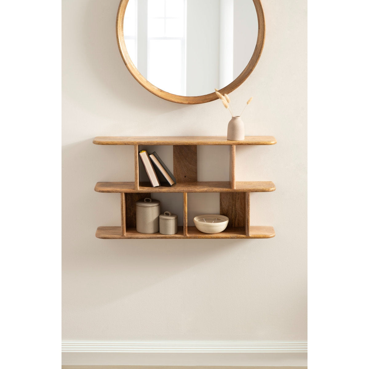 Wooden shelf with decorative items against a beige wall with a round mirror.