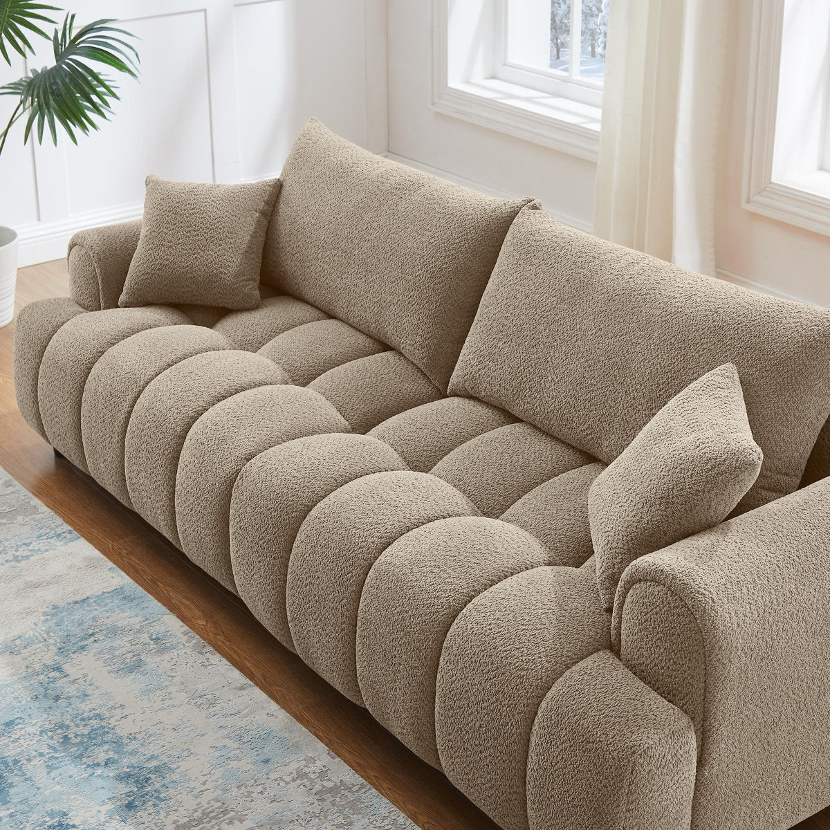 Beige sofa with cushions in a bright room with windows and a plant.