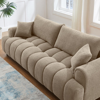 Beige sofa with cushions in a bright room with windows and a plant.