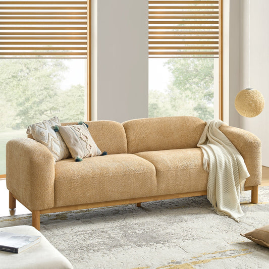 Beige sofa with decorative pillows and a blanket in a bright room with large windows.