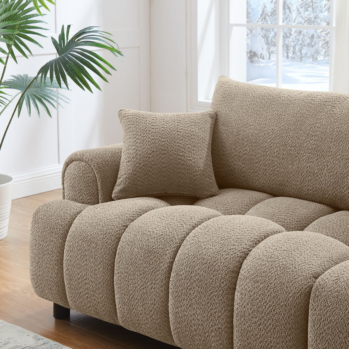 Beige textured sofa with a pillow in a bright room with a window and plant.