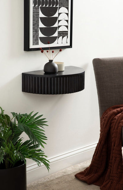 Black corner shelf with decorative items against a white wall, featuring a plant and a chair.