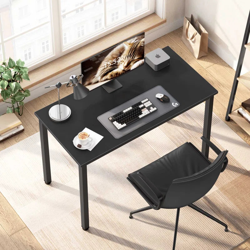Black desk with office items in a bright room.