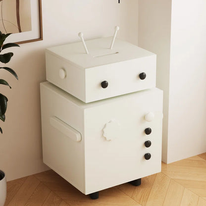 A white finished sheesham wood bedside table with one drawer and one cabinet, on casters, against a wall with a plant and decorative items in the background.