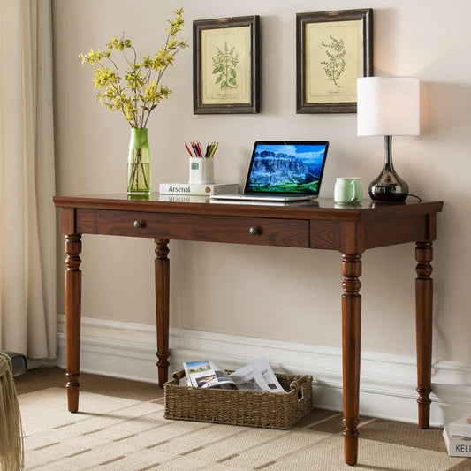 Elegant wooden writing desk with two drawers, a laptop on it, and a vase with flowers to the side, set against a wall with two framed pictures above it.