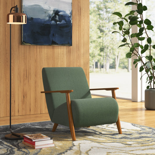 Green armchair in a living room with a plant and books on a rug.