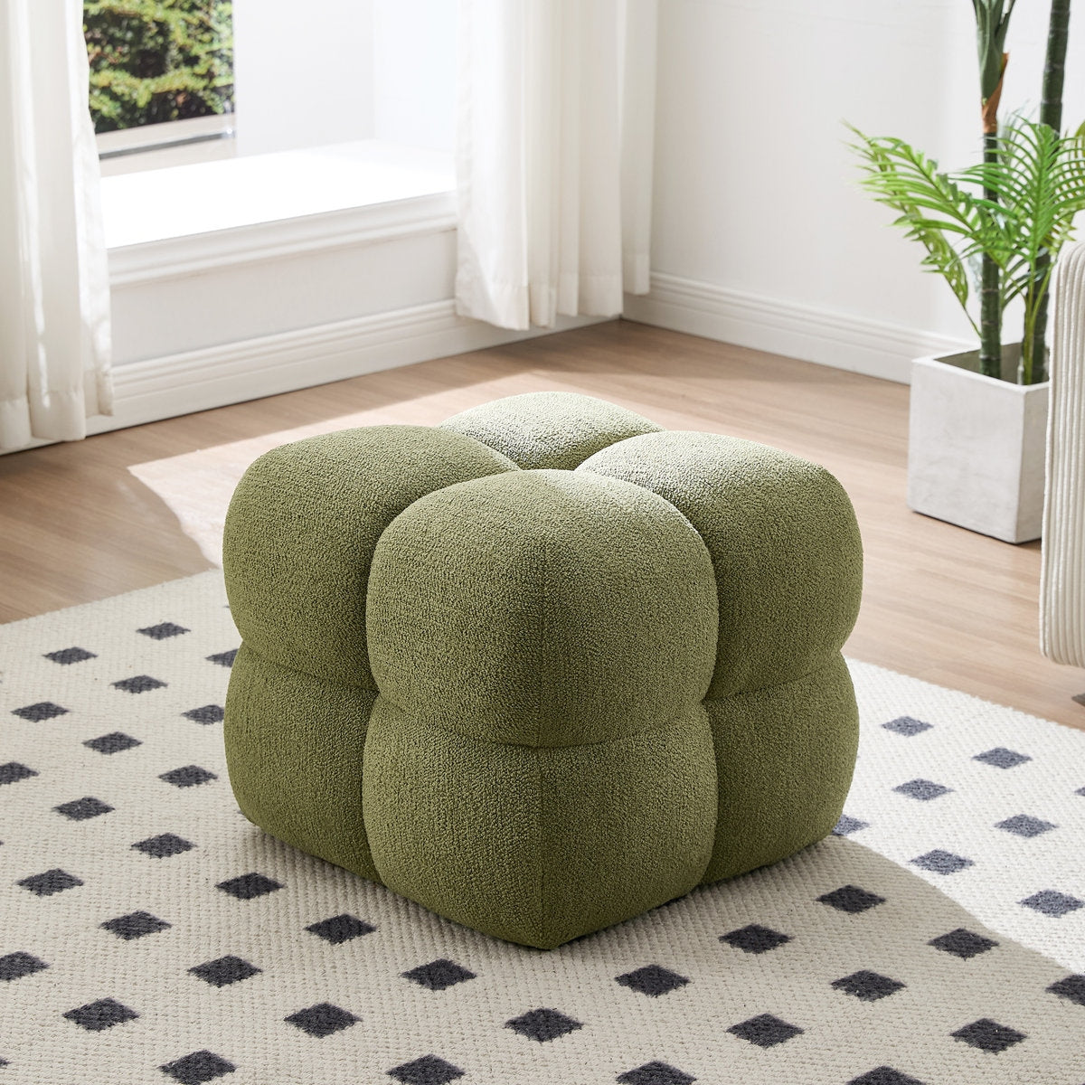 Green cube-shaped ottoman in a room with a patterned rug and window.
