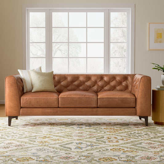 Brown leather sofa in a living room with a large window and decorative rug.