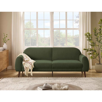 Green sofa in a living room with large windows and decor elements.