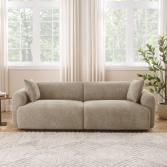 Beige sofa in a living room with large windows and a plant.