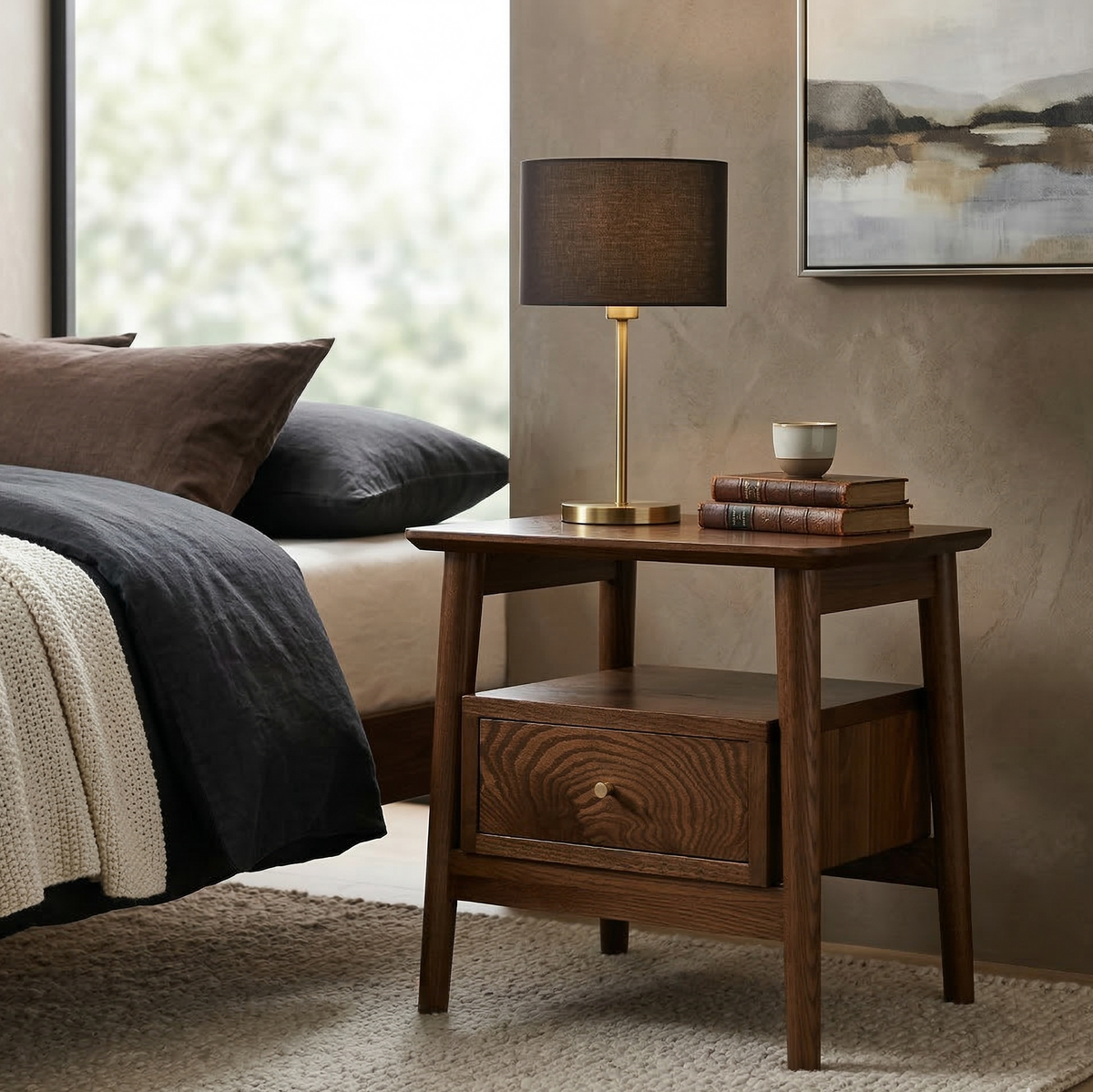 Wooden side table with lamp and books next to a bed in a bedroom.