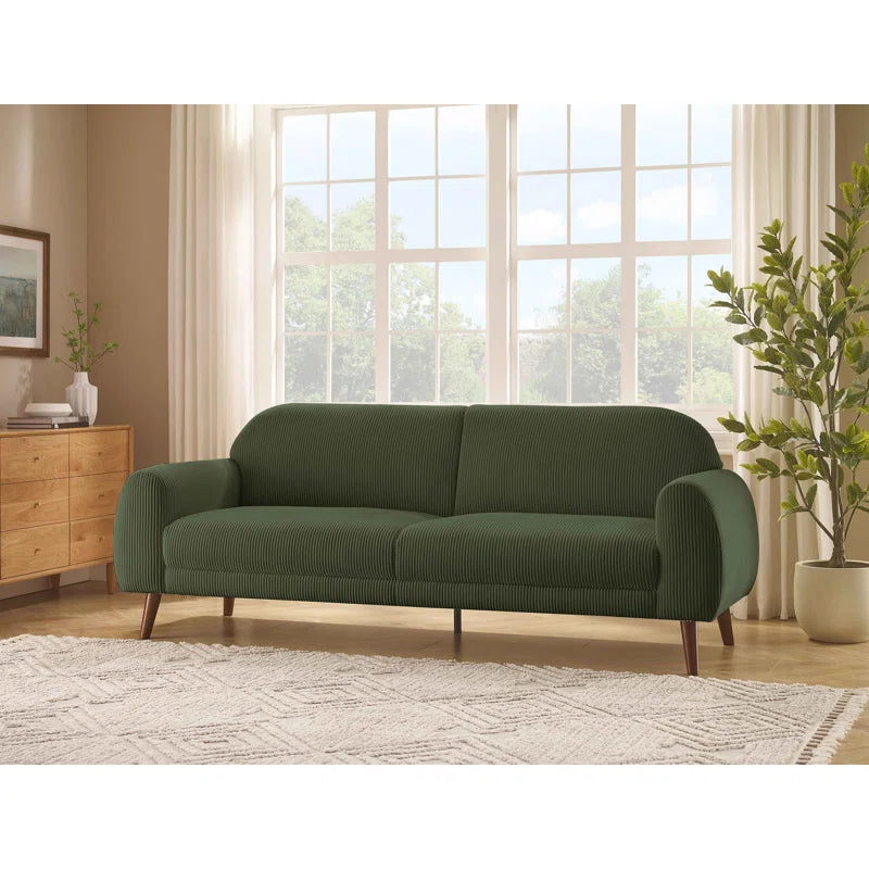 Green sofa in a living room with large windows and decor elements.
