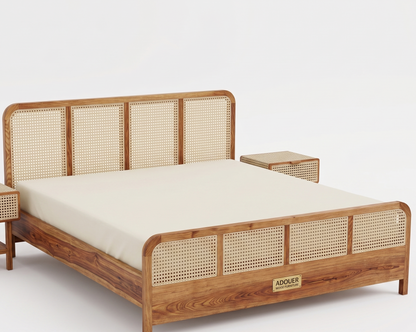 A wooden bed frame with woven cane panels, shown with a cream mattress and a matching side table on a clean white background. A gold brand plaque on the footboard reads ADOUER.
