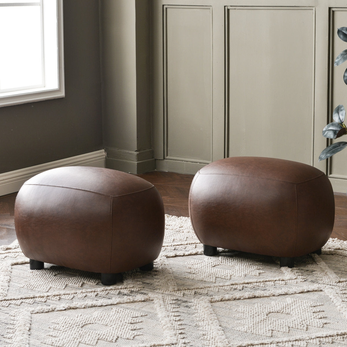 Two brown leather ottomans on a patterned rug in a room with neutral walls.