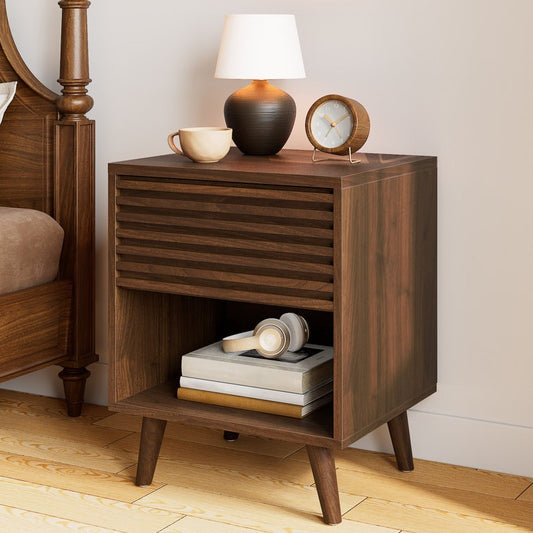 Wooden nightstand with lamp, cup, and books in a bedroom setting