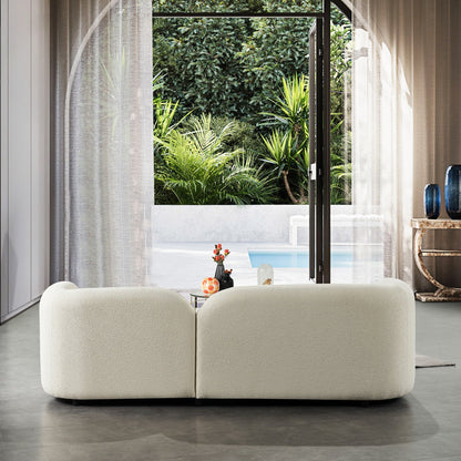 Modern white sofa in a room with large windows showing a garden and pool.