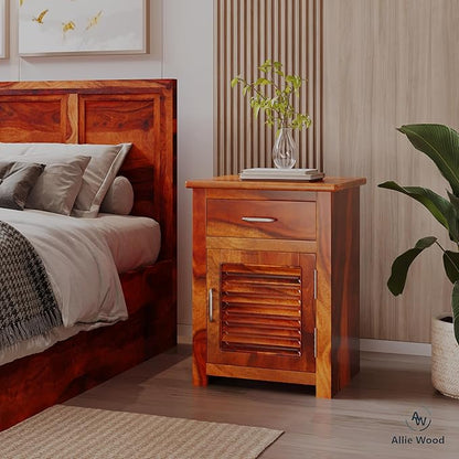 Wooden nightstand next to a bed with a plant and decorative items in a bedroom setting.