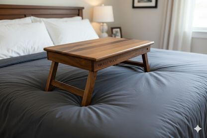 Wooden lap desk on a bed with gray bedding and a lamp in the background.