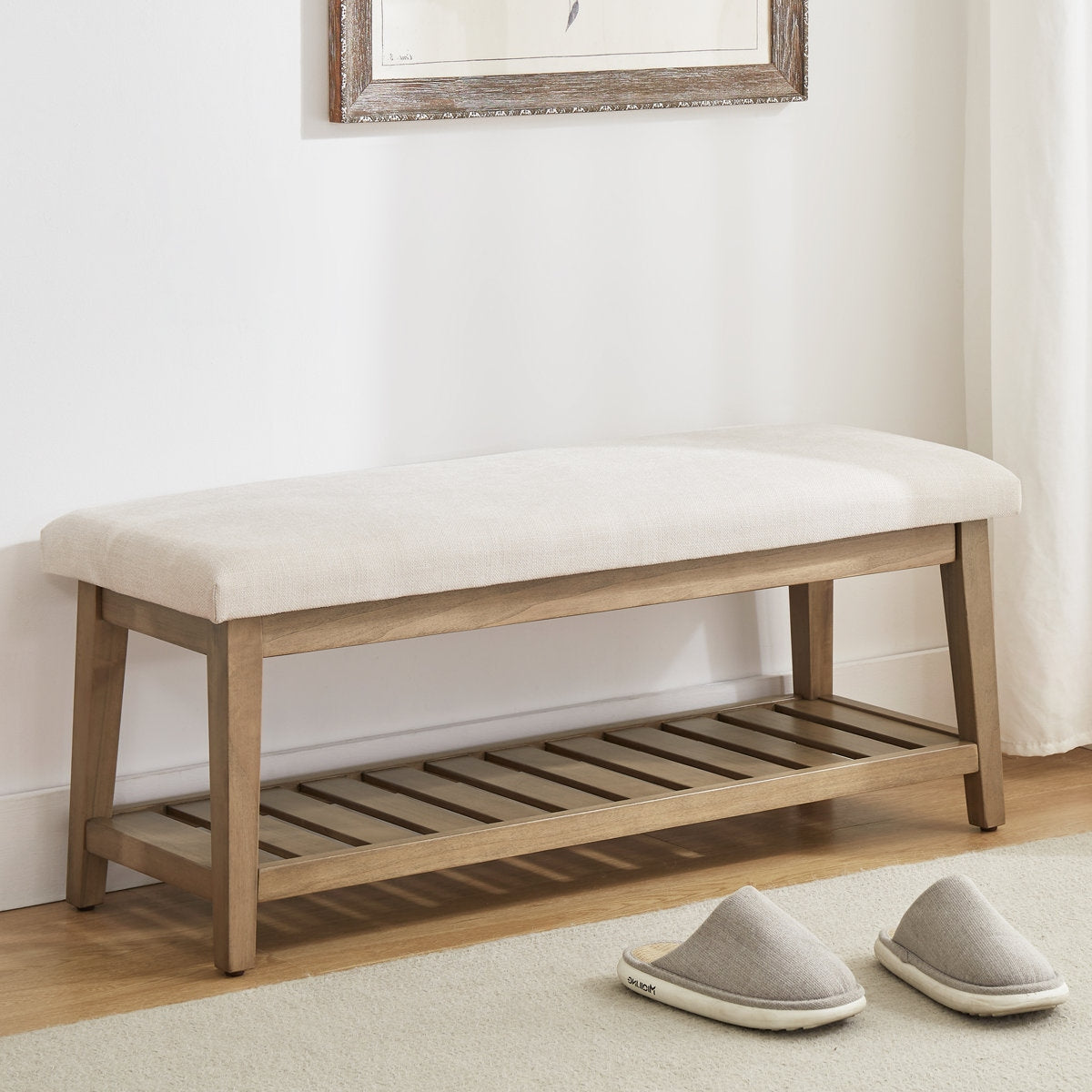 Wooden bench with white cushion on a light wooden floor, with slippers in front.
