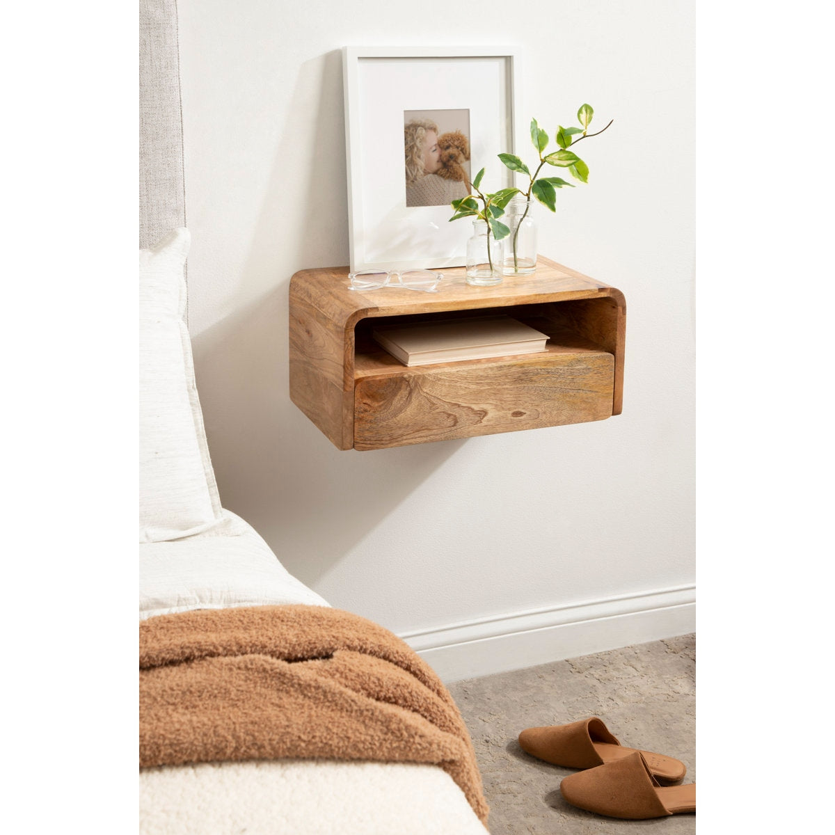 Wooden nightstand with a plant and photo frame against a white wall.