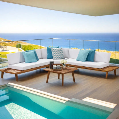 Outdoor patio set with white cushions and blue pillows by a pool with ocean view.