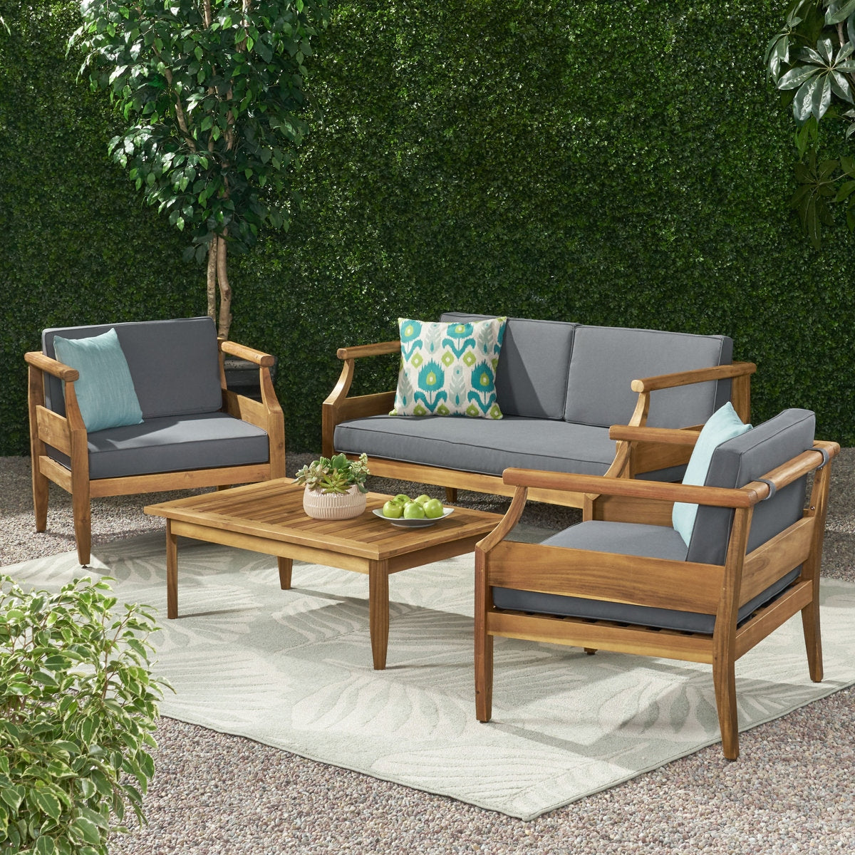 Outdoor patio set with wooden frames and gray cushions against a green hedge background.