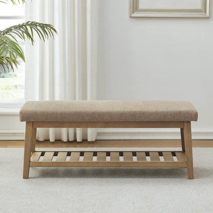 Beige upholstered bench with wooden frame in a room with white curtains and a plant.