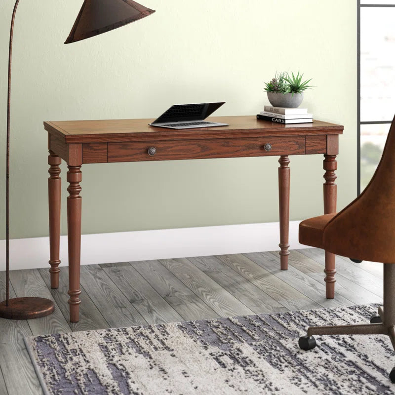 Wooden desk with a laptop and plant in a room with a green wall and wooden floor.