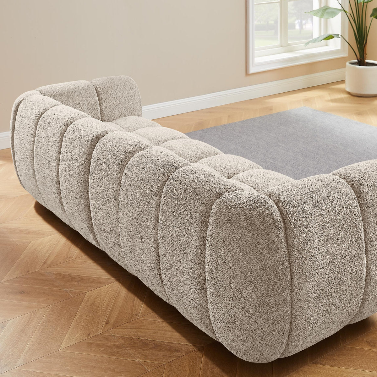 Beige tufted sofa in a room with wooden flooring and a window.