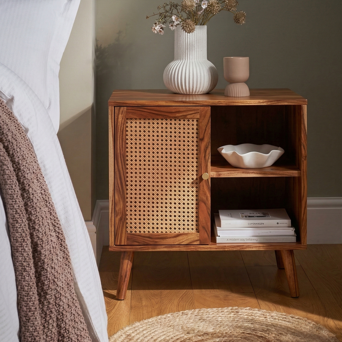 Wooden nightstand with wicker door next to a bed