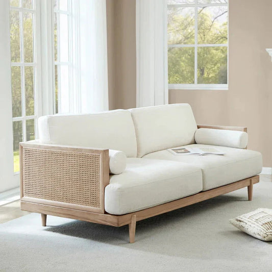 A cream upholstered three-seater sofa with solid wood cane frame, positioned in a well-lit room with a light color scheme.