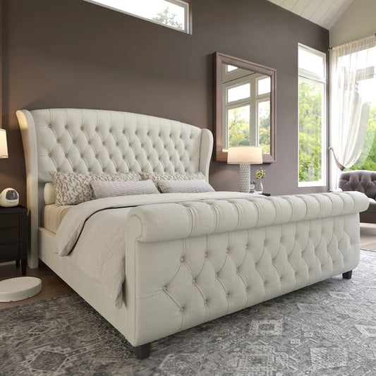 Beige tufted bed in a bedroom with a mirror and window.