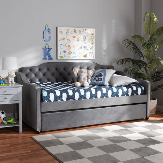 Gray upholstered bed with blue and white patterned bedding in a room with a checkered rug and plants.