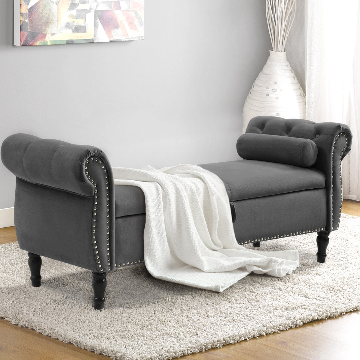 Gray upholstered bench with a white blanket draped over it in a room setting.