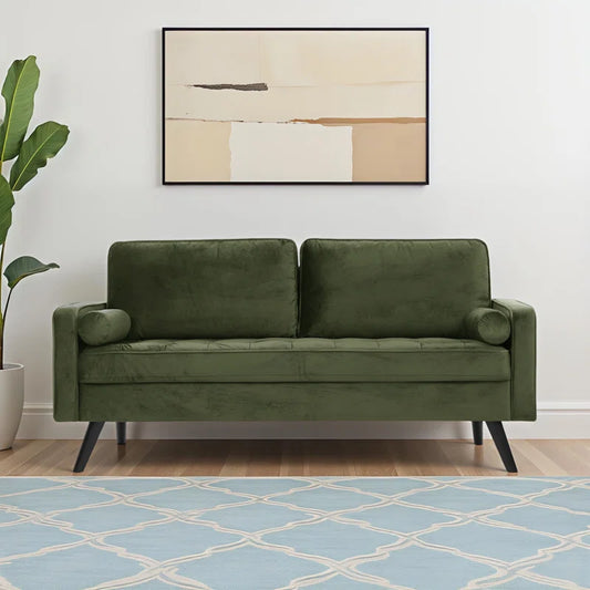 Green sofa in a living room with a abstract painting on the wall and a blue patterned rug.
