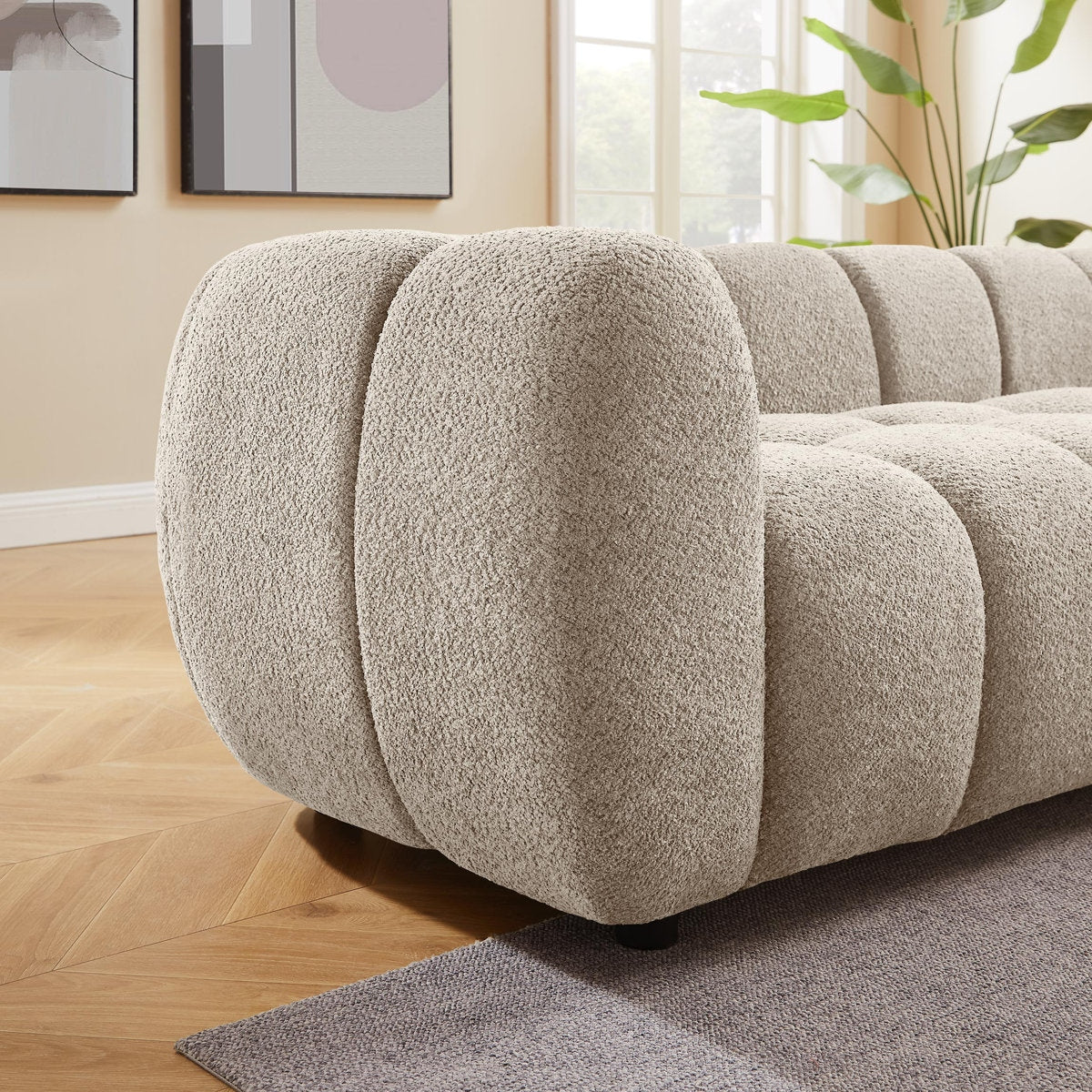 Beige textured sofa in a living room setting with light wood flooring and a plant.