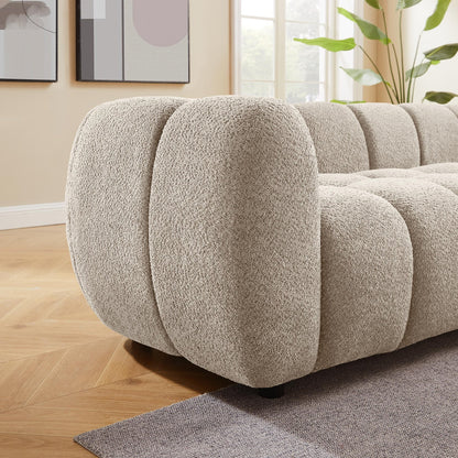 Beige textured sofa in a living room setting with light wood flooring and a plant.