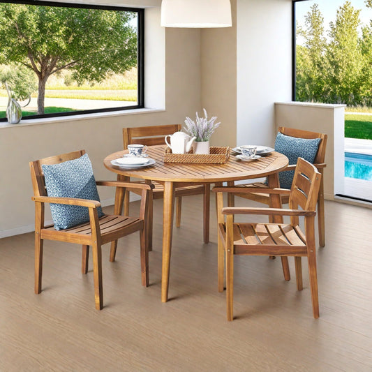 Wooden dining set with chairs and table in a room with large windows showing greenery outside.