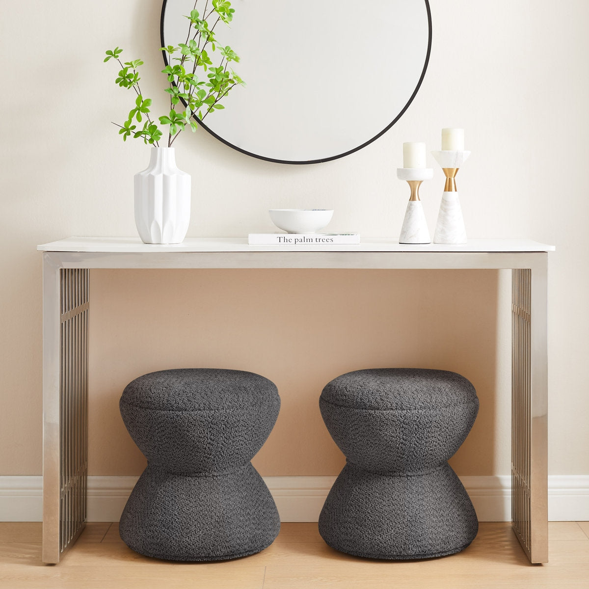 Two gray stools in front of a white table with decorative items on a beige wall.