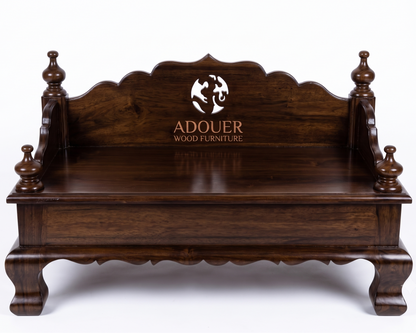 A dark brown wooden bench with ornate carved details, turned legs, and a high arched backrest featuring the 'ADOUER WOOD FURNITURE' logo, shown on a white background.