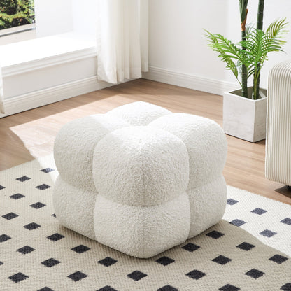 White textured ottoman on a patterned rug in a room with a plant and window.