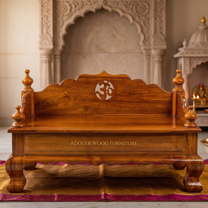 A polished reddish-brown wooden puja chowki with ornate carved details, shown in front of a decorative stone archway. The front panel reads 'ADOUER WOOD FURNITURE'.