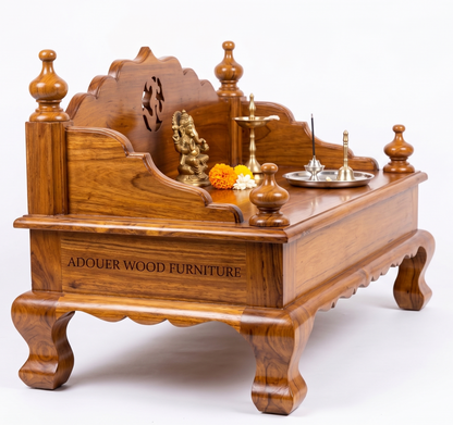 A carved wooden Shiva Panchamala altar, made of rich reddish-brown wood with 'ADOUER WOOD FURNITURE' engraved on the front panel. The altar is styled with a brass Ganesha statue, marigolds, a brass lamp, and a silver tray, set against a clean white background.