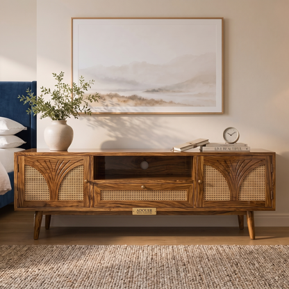 A mid-century modern wooden TV stand or media console with woven cane panels, styled in a bedroom setting under a framed landscape print.