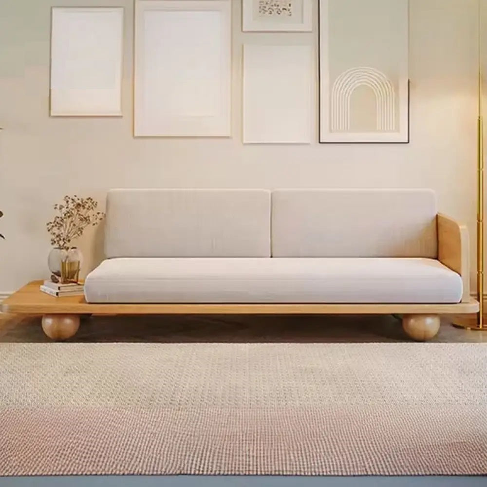 Sofa with wooden frame and white cushion in a room with framed pictures on the wall.