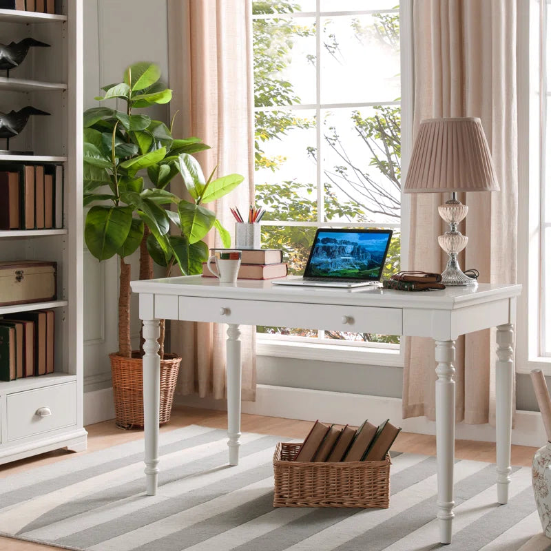 Elegant wooden writing desk with two drawers, a laptop on it, and a vase with flowers to the side, set against a wall with two framed pictures above it.