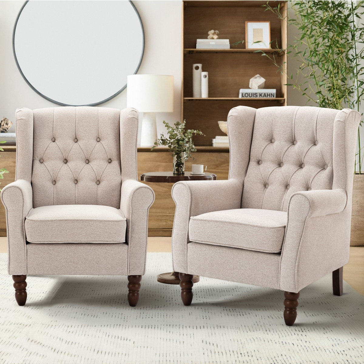 Two beige armchairs in a living room setting with a bookshelf and decor items.