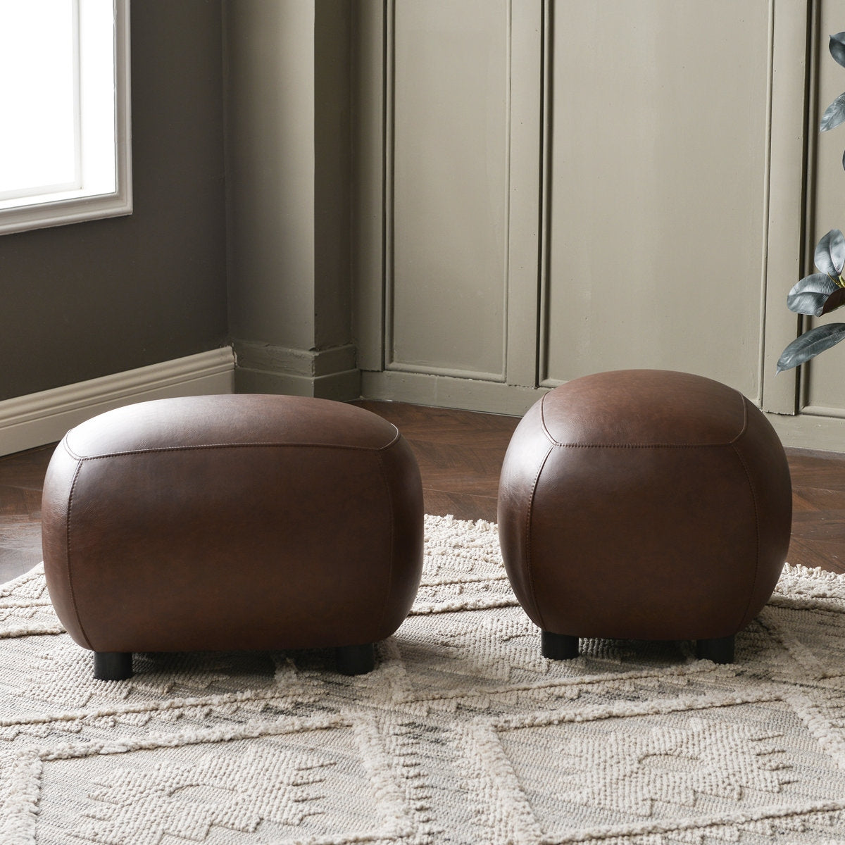 Two brown leather ottomans on a textured rug in a room with neutral walls.